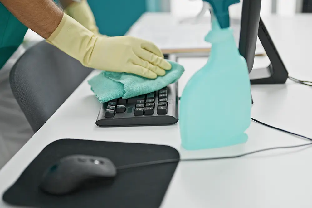 Junger Mann reinigt Tastatur mit einem Tuch im Büro